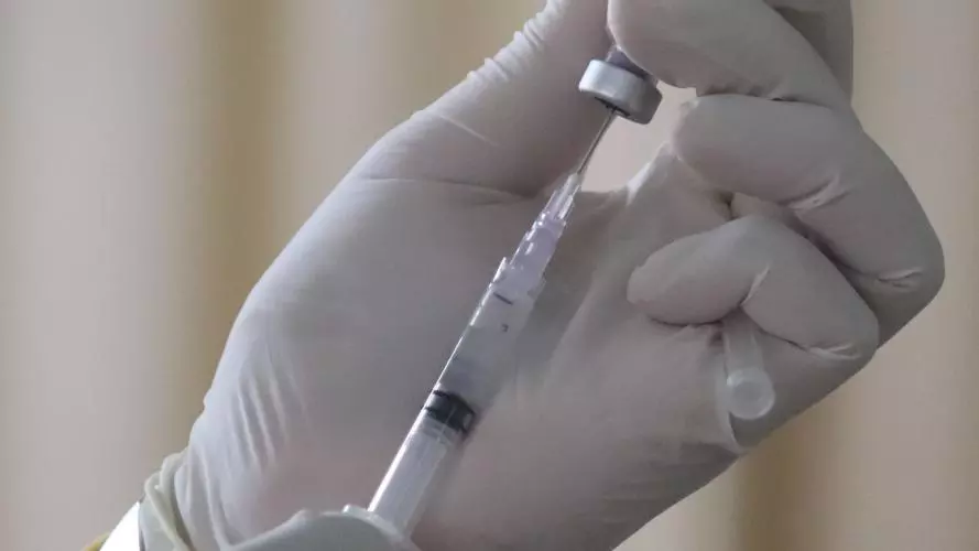 Hands wearing white gloves holding a syringe and bottle