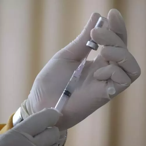 Hands wearing white gloves holding a syringe and bottle